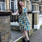 Woman in a blue floral breastfeeding dress standing on a street with a building in the background